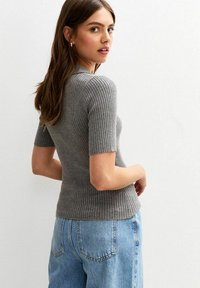 Graues geripptes Strickoberteil mit kurzen Ärmeln in taillierter Passform, kombiniert mit hoch geschnittenen hellblauen Jeans. Die Textur ist sichtbar und glatt.