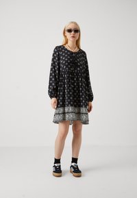 Μαύρο φόρεμα με λευκά γεωμετρικά σχέδια, σε άνετη γραμμή, μακριά μανίκια και φούστα με δαντελένια τερματισμό. Συνδυασμένο με μαύρες κάλτσες και πλατφόρμες sneakers.