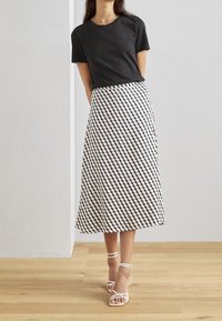T-shirt noir à manches courtes associé à une jupe mi-longue présentant un motif géométrique noir et blanc. Sandales blanches à brides.