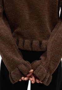 Brązowy sweter dziany o miękkiej fakturze, z prążkowanym wykończeniem i oversize'owymi mankietami, które częściowo zakrywają dłonie.