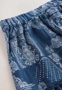 Niebieska tkanina z białym wzorem paisley oraz geometrycznymi motywami, posiadająca elastyczny pas i miękką, lekką teksturę.