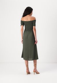 Olivgrön klänning med blottade axlar, smockad byst, figursydd midja och flödande midilång kjol. Matchad med ljusbeige remsandaler.