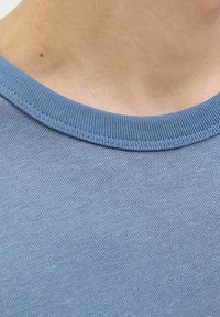Svijetloplavi pamučni majica s okruglim izrezom i rebrastim ovratnikom. Glatka tekstura s jednoličnom bojom i bez vidljivih uzoraka ili logotipa.