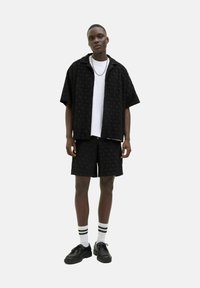 Black short-sleeve shirt and matching shorts feature a textured wave pattern. Worn with a white t-shirt, black shoes, and striped socks.