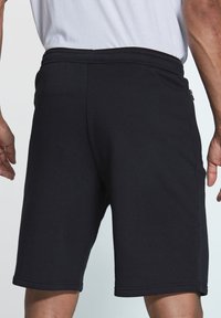Schwarze Baumwollshorts mit bequemer Passform, seitlichen Reißverschlusstaschen und einem elastischen Bund. Der Stoff hat eine glatte Textur und ist knielang.