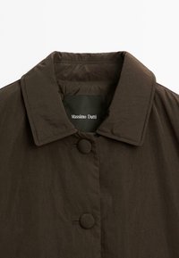Veste extérieure marron avec col rabattu, deux boutons ronds et un tissu texturé, portant une étiquette avec l'inscription "Massimo Dutti".