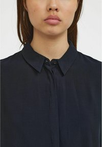 Námořnická modrá košile s klasickým límcem, zapínáním na knoflíky a jemnou, hladkou texturou. Mírně volný střih s minimálním detailem.