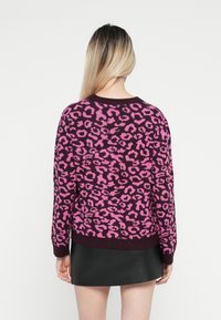 Maglione viola con stampa leopardata rosa, texture lavorata a maglia, scollo rotondo e polsini a costine. Indossato con una gonna nera per creare un contrasto.
