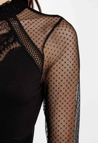 Black bodysuit featuring sheer mesh long sleeves with a polka dot pattern, rounded neckline, and lace trim details.