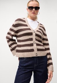 Καφέ και μπεζ ριγέ ζακέτα με V-λαιμόκοψη, κλείσιμο με κουμπιά και μπροστινές τσέπες. Μαλακή υφή με ραβδωτές μανσέτες και στρίφωμα.