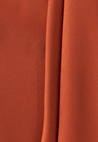 Rust-colored fabric with a smooth texture, featuring folds that create a soft draping effect. No visible patterns or hardware.