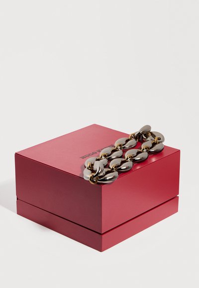Ερυθρό κουτί Hugo Boss με λαμπερό ασημένιο και χρυσό παχύ αλυσίδα βραχιόλι που ακουμπά πάνω του, εμφάνιση σε λευκό φόντο.