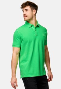 Grønn polo-skjorte laget av bomull, med klassisk krage, korte ermer og en diskret logo på brystet. Glatt tekstur og figursydd design.