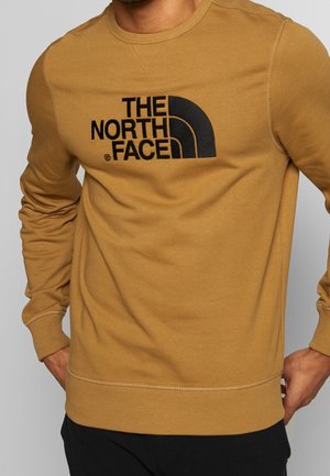 Brązowa bluza z czarnym haftowanym logo "The North Face" oraz prążkowanym wykończeniem mankietów i dołu. Gładka tekstura z okrągłym dekoltem.