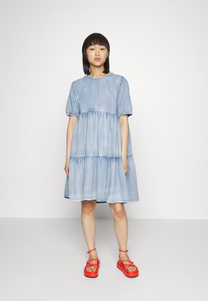 Vestido de ganga de manga curta com um corte solto, design em camadas, cor azul clara e cintura franzida, combinado com sandálias vermelhas vibrantes de tiras.