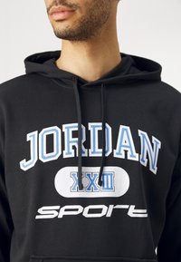 Felpa nera con cappuccio caratterizzata da grafiche bianche e azzurro chiaro: testo "JORDAN XXIII" e "sport"; tessuto texturizzato con lacci visibili.