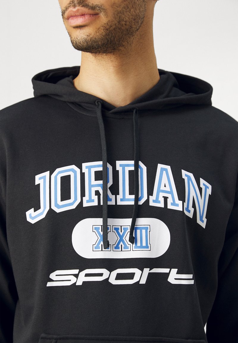 Sudadera con capucha negra que presenta gráficos en blanco y azul claro: texto "JORDAN XXIII" y "deporte"; tejido texturizado con cordones visibles.