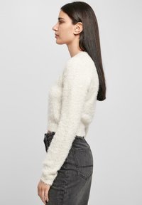 Gekürzter, flauschiger weißer Pullover mit langen Ärmeln, gerippten Bündchen und runder Ausschnitt, kombiniert mit hoch geschnittenen, dunkelgrauen Jeans.