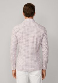 Button-up shirt van lichte stof, met een klein geometrisch patroon in roze en marineblauw op een witte achtergrond; lange mouwen en puntige kraag.