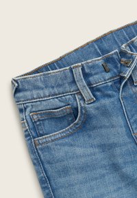 Jeans in denim azzurro chiaro con un tradizionale design a cinque tasche, cuciture arancioni a contrasto e chiusura con bottoni in vita.