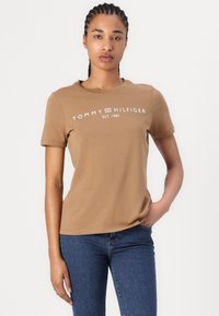 Hnědé bavlněné tričko s krátkým rukávem, kulatým výstřihem a bílým potiskem "TOMMY HILFIGER EST. 1985" na přední straně. Klasický střih.