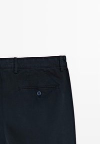 Vue arrière d'un pantalon bleu marine foncé montrant la ceinture, les passants de ceinture et une seule poche arrière avec bouton.