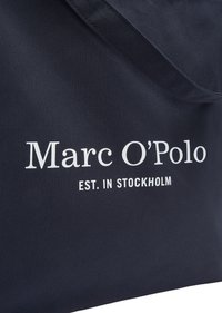 Tissu bleu foncé avec le texte blanc « Marc O'Polo » et « EST. À STOCKHOLM » imprimé en surface.