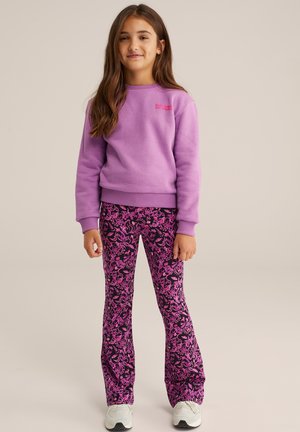 Paarse sweater met ronde hals en geribbelde manchetten; roze bloemenpatroon wijde broek; witte sneakers; neutrale achtergrond.