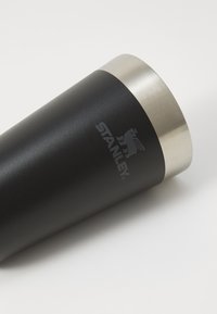 Black stainless steel tumbler with a brushed silver rim. Features the "STANLEY" logo in gray. Smooth texture and tapered design.