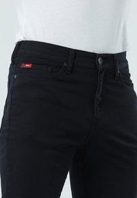 Schwarze Denim-Jeans mit geradem Bein, fünf Taschen-Design und einem kleinen roten Logo-Tag auf der vorderen Tasche. Robuste Stofftextur.