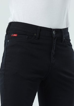 Jean en denim noir avec une coupe droite, design à cinq poches et une petite étiquette logo rouge sur la poche avant. Tissu durable.