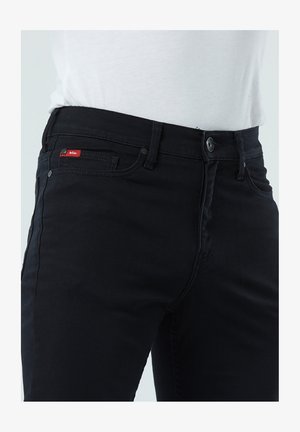 Jean en denim noir avec une coupe droite, design à cinq poches et une petite étiquette logo rouge sur la poche avant. Tissu durable.