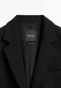 Blazer nero con revers a punta, caratterizzato da una texture di tessuto liscia. Etichetta del marchio visibile all'interno, con la dicitura "Massimo Dutti, Made in Portugal."