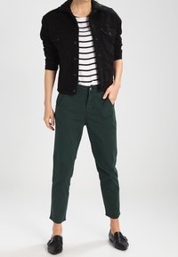 Veste en denim noire avec col en sherpa, t-shirt rayé blanc et marine, chinos verts et chaussures noires à enfiler. Style décontracté et ajusté.