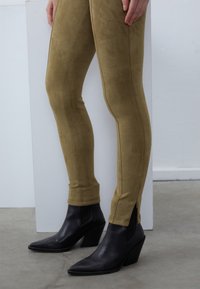 Beige faux suede leggings med sideslits, kombinert med svarte spisse ankelstøvler med strukturert finish og avkuttet hæl.