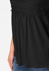 Svart blus med texturerad smockad överdel och samlad tyg nedan. Har en lös passform och rak nederkant, tillverkad av mjuk bomullsblandning.