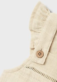 Närbild av beige linnetyg med en träknapp och rynkade kanter på en plaggsrem.