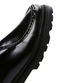 Stivale in pelle nera lucida con un design curvo, cuciture dettagliate lungo la cucitura e una suola in gomma ruvida e testurizzata.