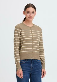 Beige cardigan med kremfargede striper, med rund hals og knappelukking, fullført med ribbestrikkede mansjetter og nederkant. Brukt sammen med blå jeans.