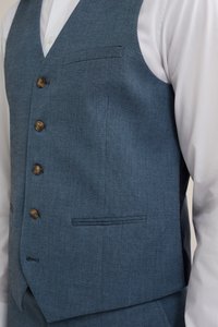 Chaleco de tweed azul para hombre con un patrón texturizado, cinco botones marrones y un bolsillo en el pecho, combinado con una camisa blanca de vestir.