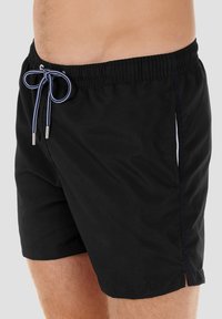 Shorts de bain noirs avec une taille élastique, un cordon de serrage, et des coutures bleues contrastantes sur les côtés. Dispose de poches latérales ouvertes.