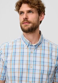 Korte mouwen, knoopshirt in lichtblauw, beige en wit geruit patroon. Bevat een borstzak en een kraag.