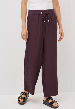 Maroon färgade vida byxor med dragsko och elastisk midja, med silveröglor och ett lätt, strukturerat tyg. Parat med svarta sandaler.
