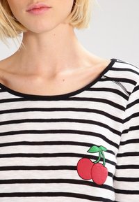 Koszulka w paski z czarno-białymi poziomymi pasami, okrągłym dekoltem i czerwoną grafiką wiśni z zielonymi liśćmi po lewej stronie.