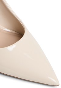 Escarpin en cuir verni beige clair, à bout pointu, avec une finition brillante et une texture lisse. Présente un design à décolleté bas.