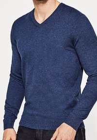 Marinblå v-ringad tröja, stickad textur, långa ärmar, figursydd design, ribbade manschetter och fåll, tillverkad av mjukt material.