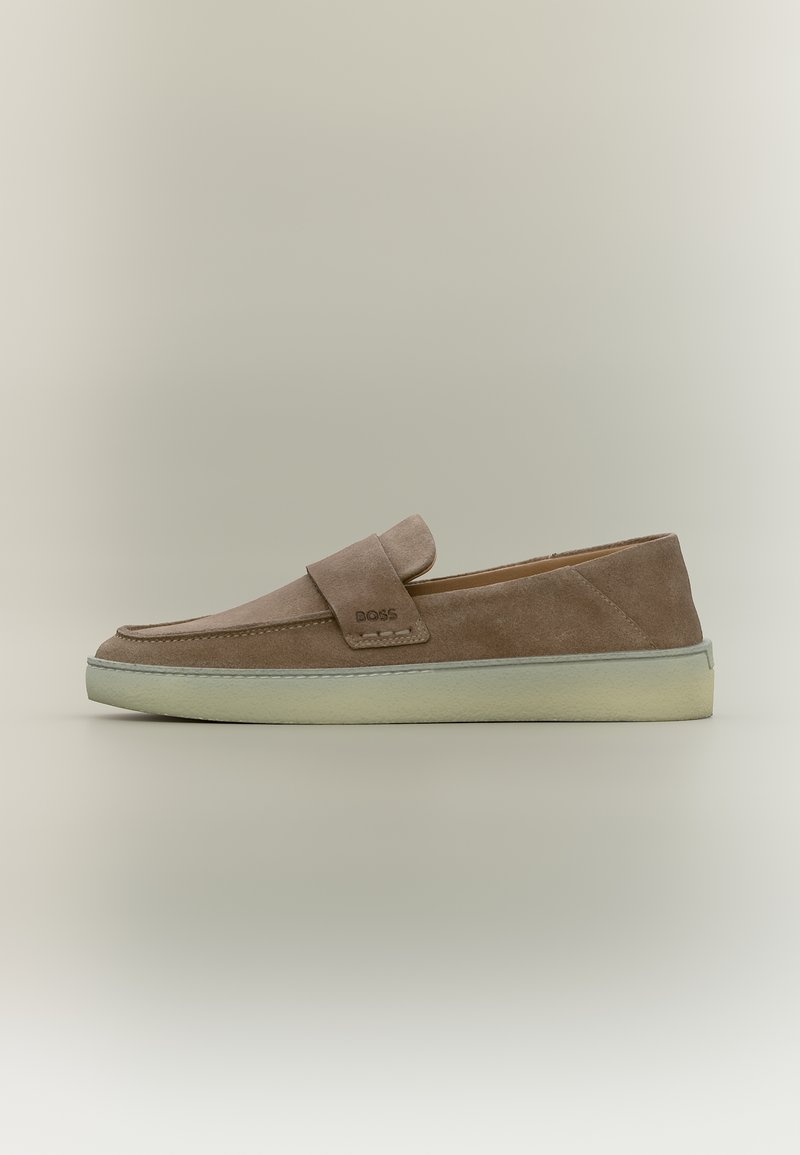 Bézs színű, velúr anyagú, könnyen felhúzható mokaszin fehér gumitalppal és a BOSS logóval az oldalsó pánton, egyszínű semleges háttér előtt bemutatva.