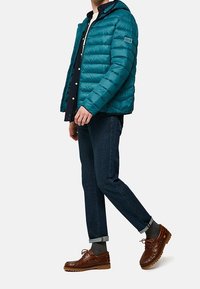 Turkos puffjacka med huva, med ett kviltat mönster, i kombination med mörka jeans och bruna snörskor. Avslappnad outfit, solida färger.