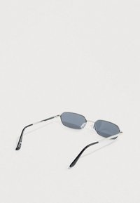 Ασημένια γυαλιά ηλίου με μεταλλικό πλαίσιο και οβάλ γκρι φακούς. Μαύροι βραχίονες από οξικό υλικό. Διαθέτουν ρυθμιζόμενα μαξιλαράκια μύτης και διακριτικό λογότυπο στο πλάι.