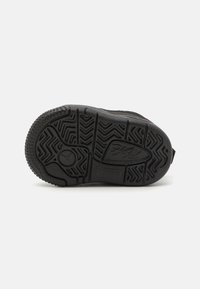 Svart sneakersåle med teksturert gummi, med herringbone-mønster, sirkulært logo og merkevaredetalj. Flat og bred form.